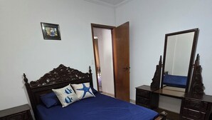Une chambre à coucher avec un lit en bois, une table de chevet, une commode, un miroir et une porte donnant sur une autre pièce.