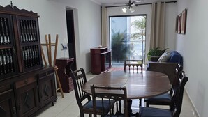 Un coin repas avec une grande table en bois, six chaises, un buffet en bois foncé, un ventilateur de plafond et une grande fenêtre avec des rideaux.