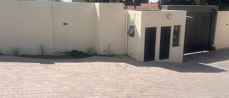 Un área de acceso pavimentada con entrada protegida por un portón y un pequeño armario de servicios.