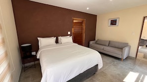 A bedroom with a bed, a sofa, a lamp, and a door.