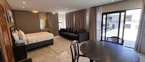Una habitación de hotel moderna con cama, sofá, mesa de comedor y ventanas amplias.