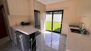A modern kitchen with a large island, a refrigerator, and a sliding glass door leading to a green outdoor area.
