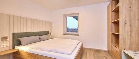 Une chambre avec un lit en bois, une table de chevet, une fenêtre et des étagères intégrées en bois.