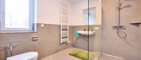 A modern bathroom with a toilet, a shower, a sink, and a window.