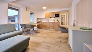 A modern kitchen with wooden cabinets, a dining area with a table and chairs, and a grey sofa. - Starnberger See Apartments (Starnberg)
