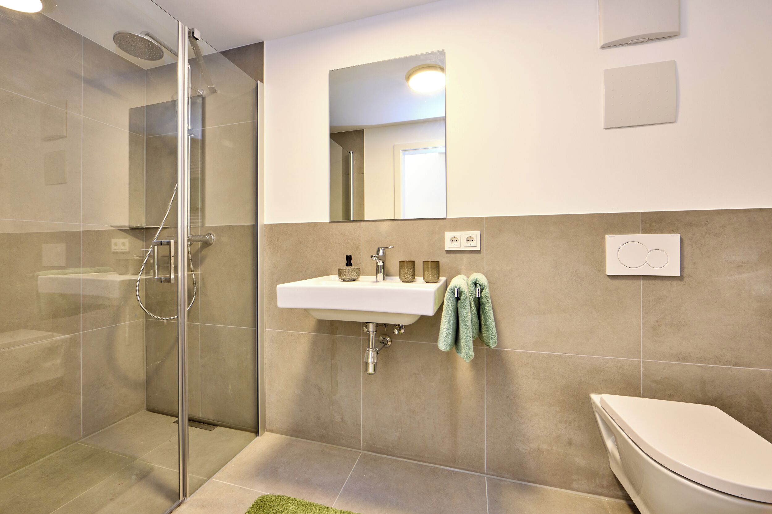 A modern bathroom with a glass-enclosed shower, a sink with a mirror above it, and a toilet.