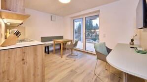 A modern kitchen with a wooden countertop, a dining area with a bench, and a large sliding glass door leading to a balcony. - Starnberger See Apartments (Starnberg)