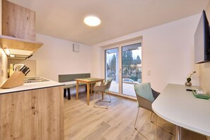 A modern kitchen with a wooden countertop, a dining area with a bench, and a large sliding glass door leading to a balcony. - Starnberger See Apartments (Starnberg)