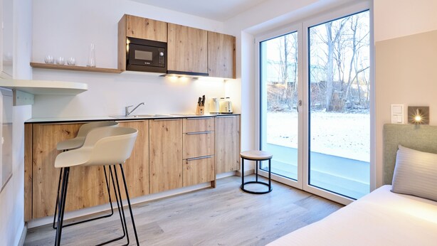 A modern kitchen with wooden cabinets, a built-in microwave, and a large window. - Starnberger See Apartments (Starnberg)
