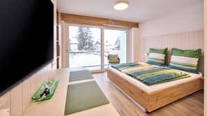 A bedroom with a bed, a TV, a sliding glass door, and a view of the outside. - Starnberger See Apartments (Starnberg)