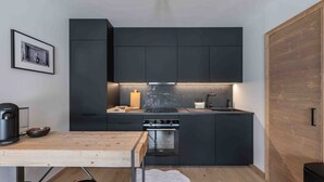 A compact kitchen with dark cabinetry, a wooden dining table, and a small island with a sink. - Renovated and bright apartment - 6 guests (Megève)