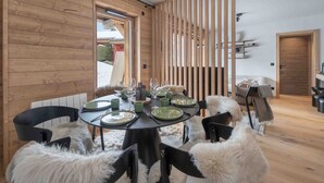 A dining area with a round table set for four, wooden paneling on the walls, and a view of the outside. - Renovated and bright apartment - 6 guests (Megève)