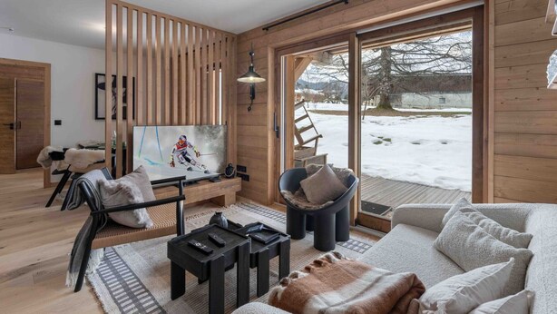 A modern living room with a ski-themed painting, a sofa, a coffee table, and a view of a snowy landscape through large sliding doors. - Renovated and bright apartment - 6 guests (Megève)