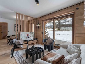 Uma sala de estar moderna com um quadro com tema de esqui, um sofá, uma mesa de centro e vista para uma paisagem nevada através de grandes portas deslizantes.