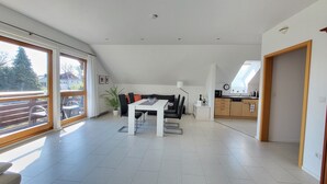 A spacious living area with a dining table, black sofa, and a view of the outdoors through large windows. - Apartment 'Dachgeschoss' with Wi-Fi (Leipzig)