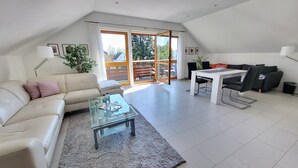 A modern living room with a sofa, a glass coffee table, a dining table with chairs, and a sliding glass door leading to an outdoor area. - Apartment 'Dachgeschoss' with Wi-Fi (Leipzig)