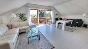 A modern living room with a sofa, a glass coffee table, a dining table with chairs, and a sliding glass door leading to an outdoor area. - Apartment 'Dachgeschoss' with Wi-Fi (Leipzig)