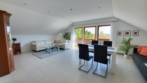 A spacious living area with a high ceiling, a dining table with chairs, a sofa, and a large window with a view of greenery. - Apartment 'Dachgeschoss' with Wi-Fi (Leipzig)