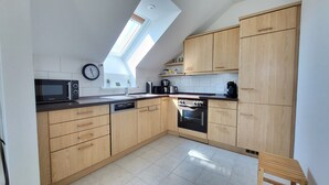 A modern kitchen with wooden cabinets, a dishwasher, a stove, and a microwave. - Apartment 'Dachgeschoss' with Wi-Fi (Leipzig)