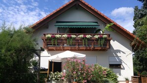 A two-story house with a balcony adorned with flowers, a covered patio, and a garden with blooming plants. - Apartment 'Dachgeschoss' with Wi-Fi (Leipzig)