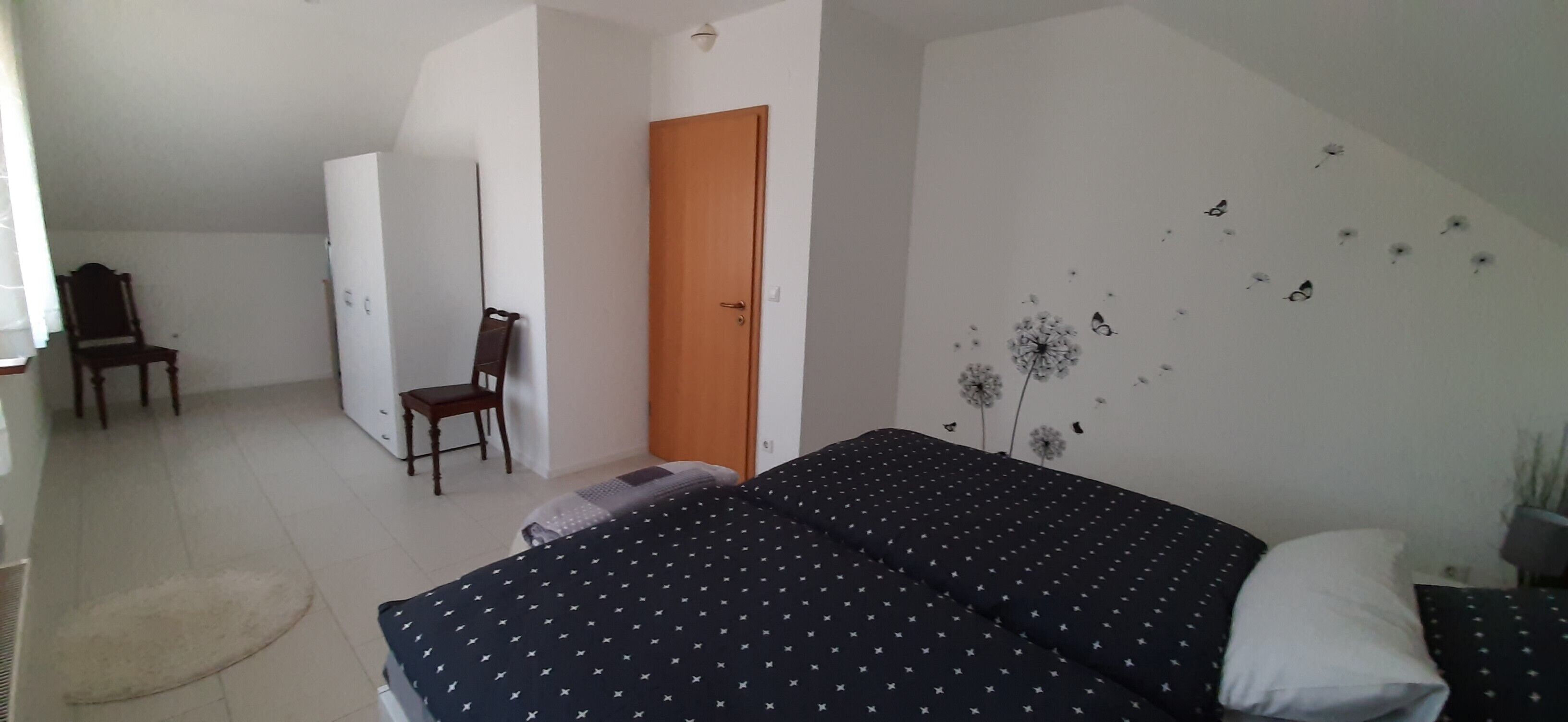A bedroom with a bed, a chair, a wardrobe, and a door.