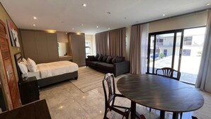 Moderni hotellihuone, jossa on sänky, sohva, ruokapöytä ja näkymä ulos.