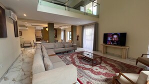 Moderni olohuone, jossa on kulmasohva, lasinen sohvapöytä ja litteänäyttöinen televisio.