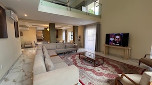Un salon moderne avec un canapé d’angle, une table basse en verre et un téléviseur à écran plat.