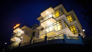 Un hôtel à plusieurs étages, doté de balcons, d’une enseigne bien visible et d’une façade bien éclairée.