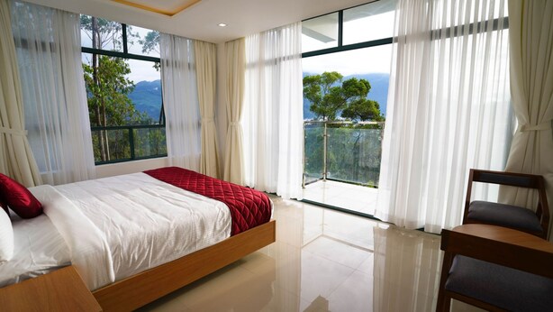 Une chambre à coucher avec un lit, une chaise et de grandes fenêtres donnant sur des arbres et des montagnes.