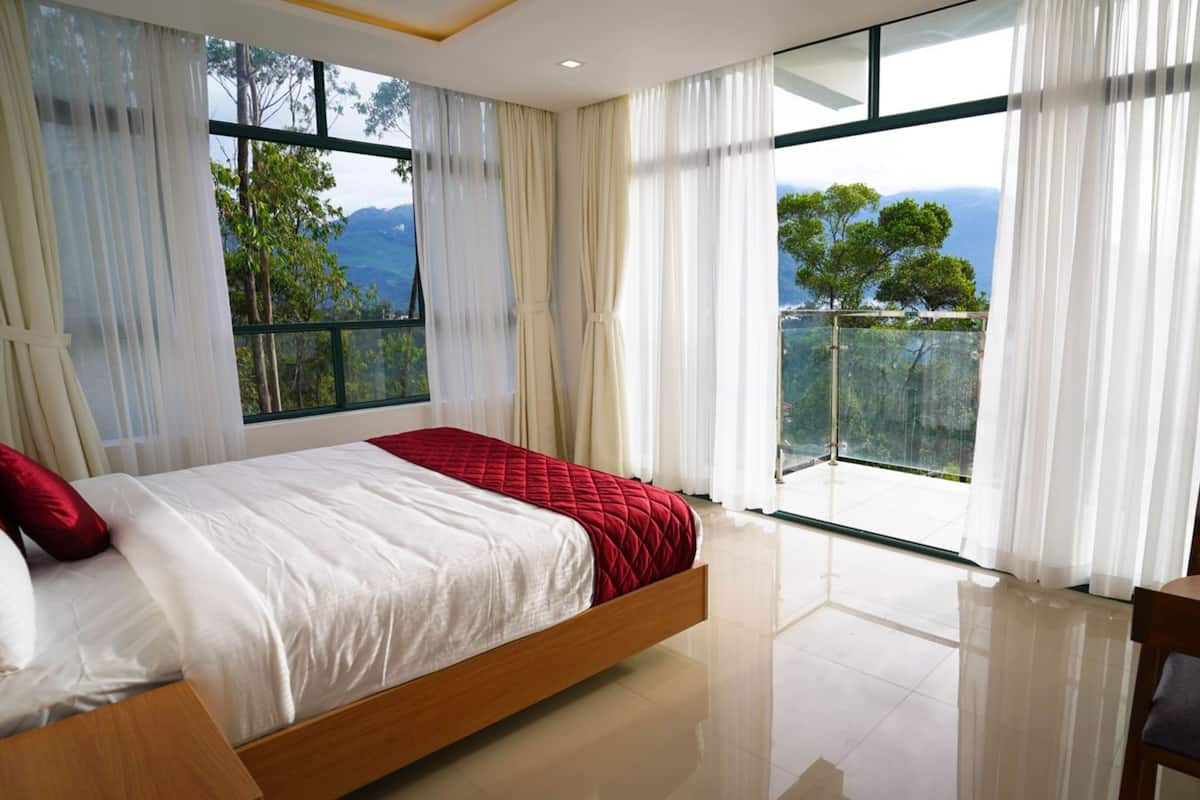 A bedroom with a bed, a chair, and large windows with a view of trees and mountains.