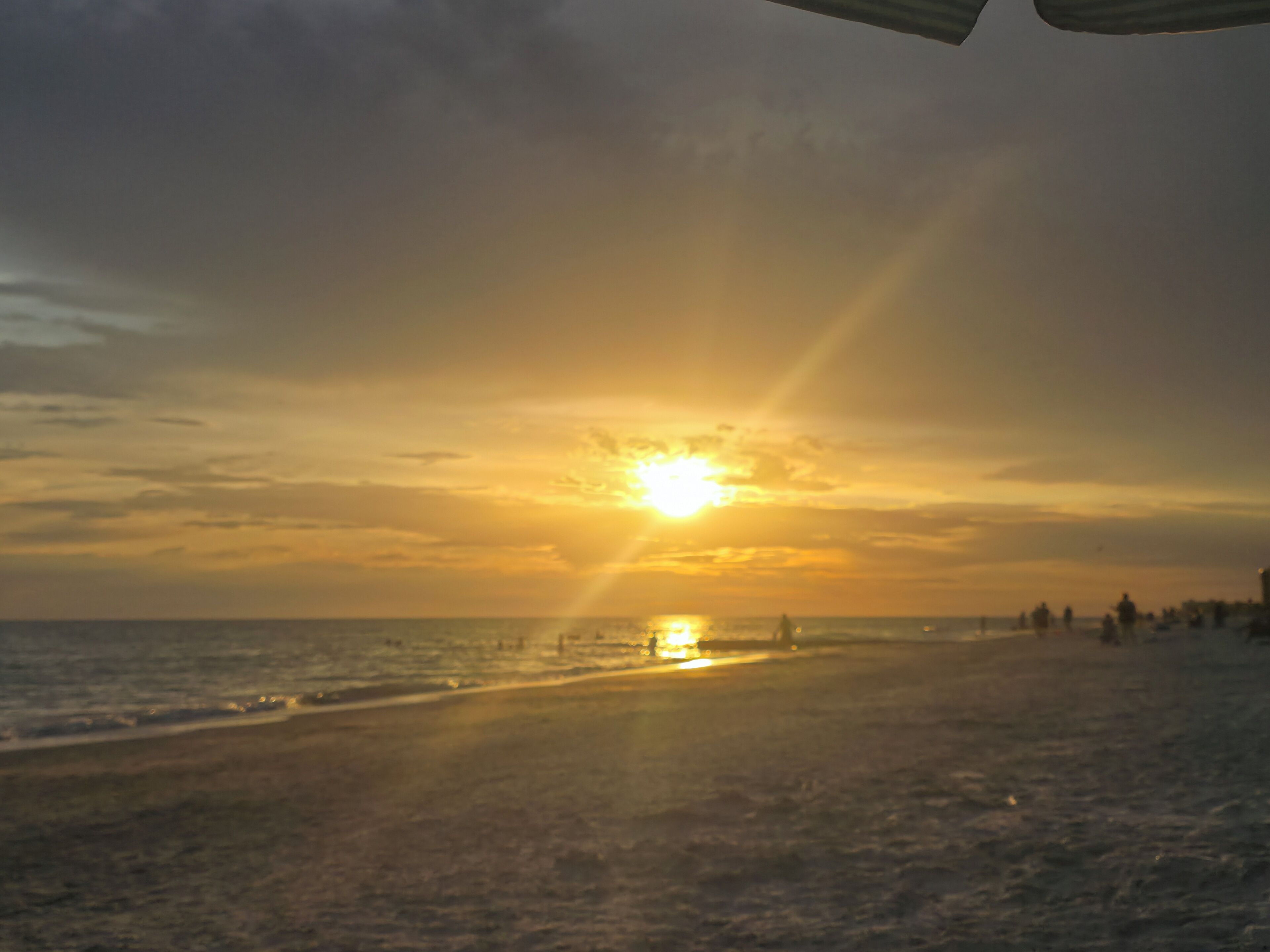 En strand med solnedgang over horisonten, der skaber en silhuet af kystlinjen.