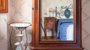 A wooden armoire with a mirror, a small table with a vase, and a bed with a blue patterned bedspread. - PALAZZO FIORENZI - DIMORA STORICA (Osimo)