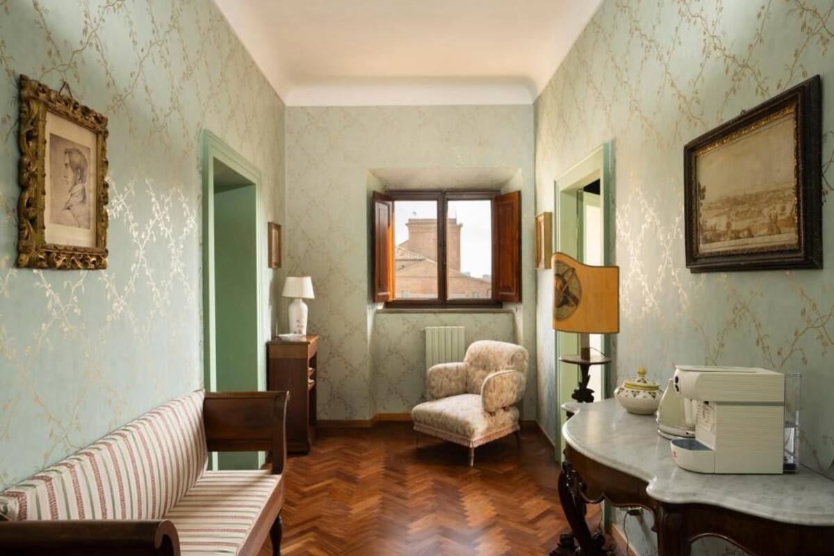 A room with a herringbone floor, a sofa, a chair, a table with a lamp, and a radiator.