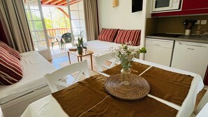 Ein Zimmer mit einem Bett, einem Esstisch mit einer Vase, einer Küchenzeile und Blick durch eine Glastür.