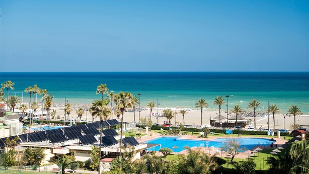 A resort with a swimming pool, beach, palm trees, and solar panels.