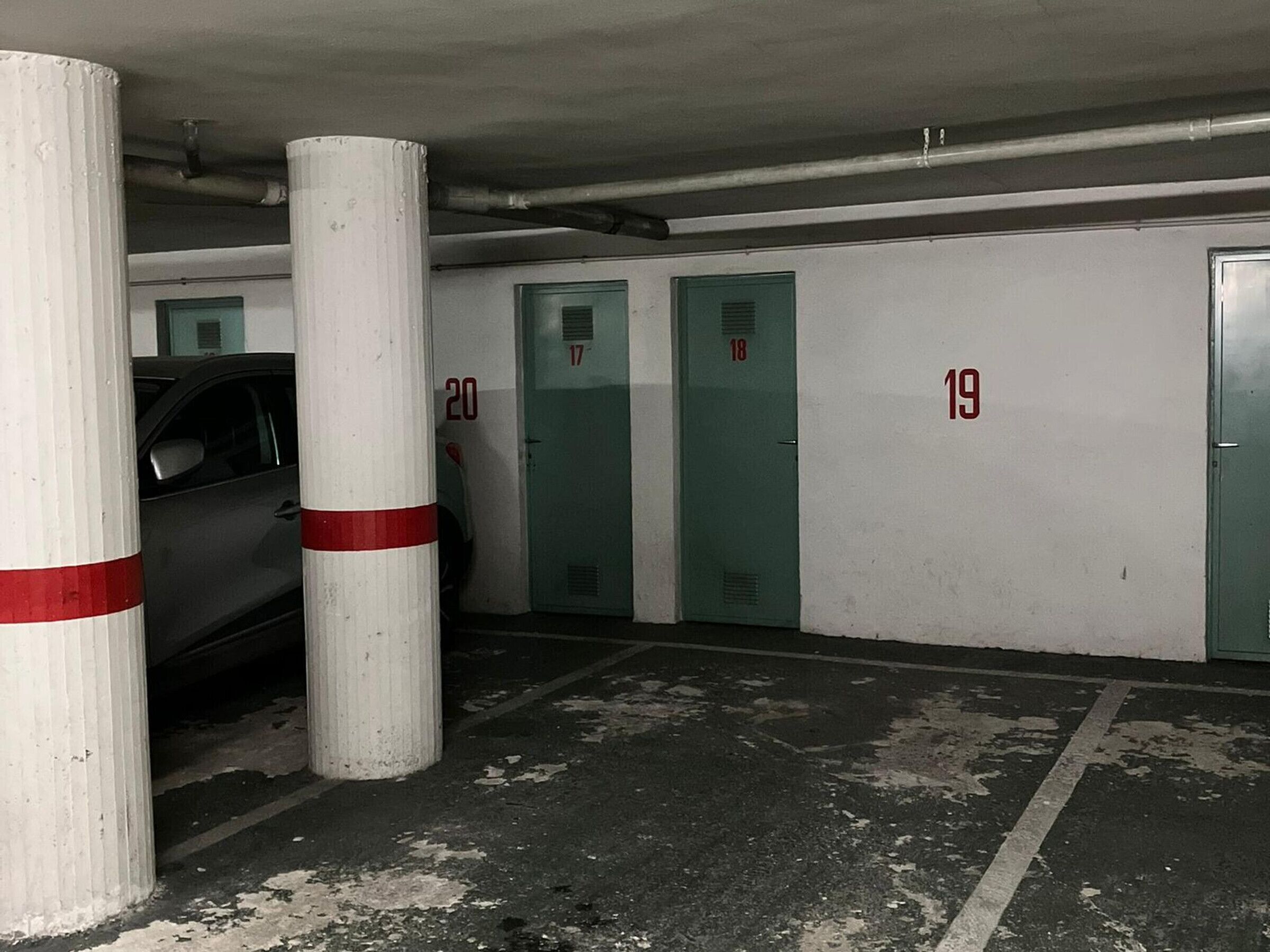Een parkeergarage met genummerde parkeerplaatsen, een auto geparkeerd op een plek en een pilaar met een rode streep.