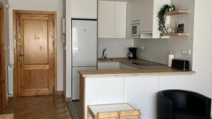 Een moderne keuken met witte kasten, een inbouwmagnetron, een koffiezetapparaat en een zwarte stoel.