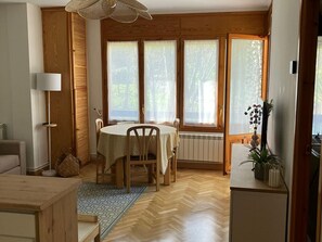 Un comedor con una mesa preparada para cuatro personas, un radiador y una ventana con cortinas.