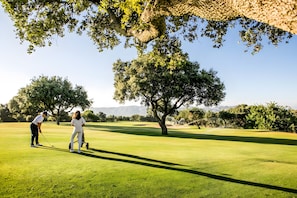 Un parcours de golf avec un ciel dégagé, des arbres et une chaîne de montagnes à l’horizon.