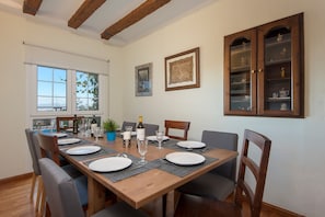 Un coin repas avec une table en bois dressée pour quatre personnes, des chaises, un buffet aux portes vitrées et une fenêtre donnant sur un beau paysage.