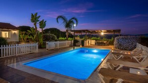 En swimmingpool med liggestole, et pergolaområde og et hvidt stakittet hegn.