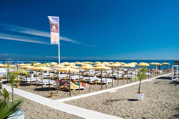 Une plage bordée de rangées de transats et de parasols, avec un drapeau et une vue dégagée sur la mer.