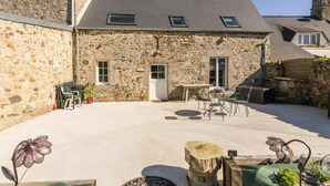 Ein Gebäude aus Stein mit einem Ziegeldach, einer kleinen Terrasse mit Gartenmöbeln und einer Tür zum Innenbereich.