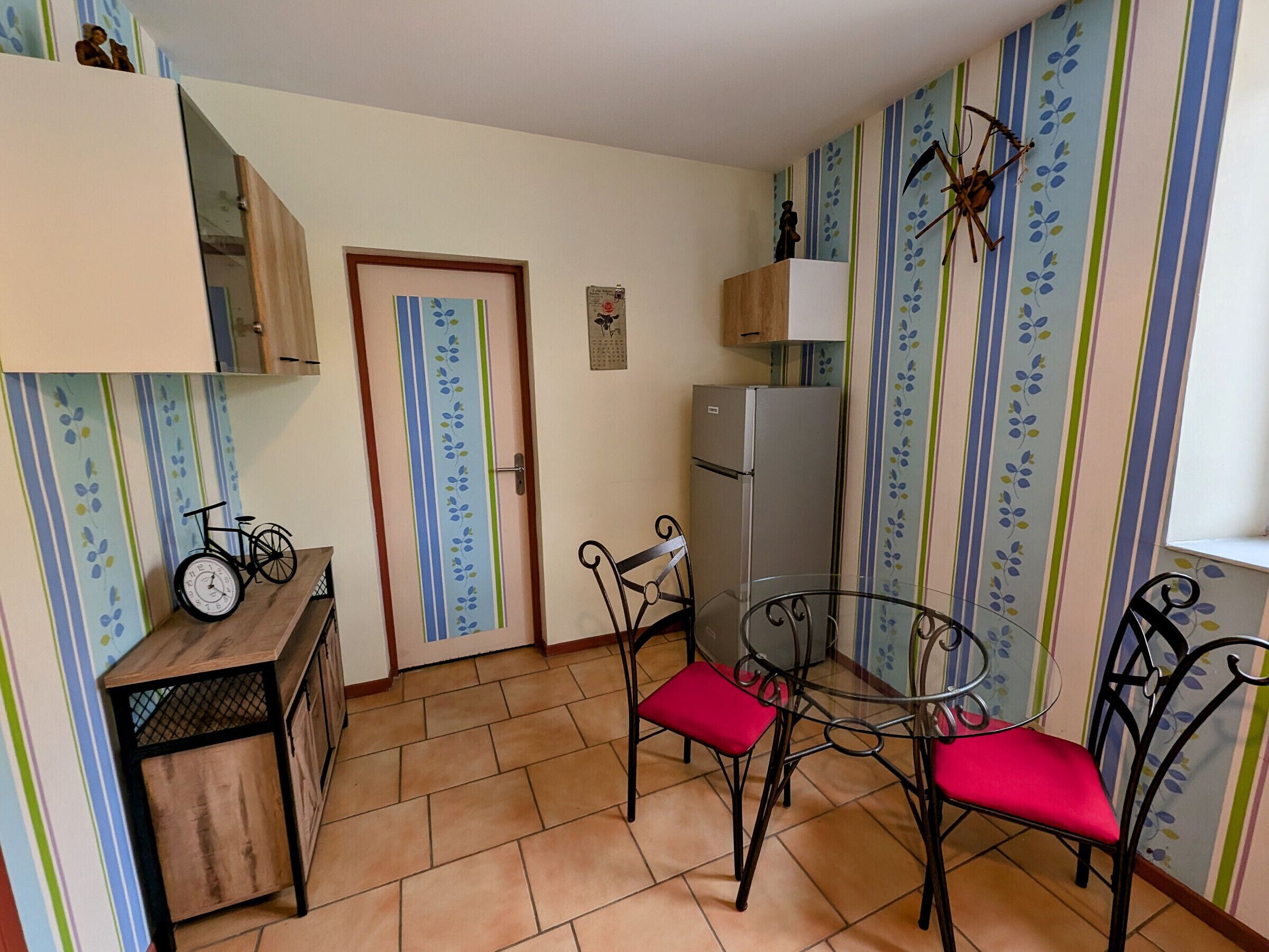 Una cocina compacta con refrigerador, una mesa de comedor con sillas y un pequeño armario.
