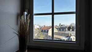 A room with a large window offering a view of buildings and a church steeple. - Urban house, air conditioning, pets welcome – 6 guests (Moulins)