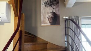 A wooden staircase with a metal handrail, a wall-mounted painting of a vase with a tree, and a window with curtains. - Urban house, air conditioning, pets welcome – 6 guests (Moulins)