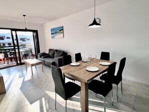A modern dining area with a wooden table, black chairs, and a view of the city through large windows.