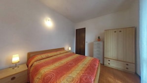 A bedroom with a bed, bedside lamps, a wardrobe, and a door. - Spacious Apartment With two Balconies (Lignano Sabbiadoro)