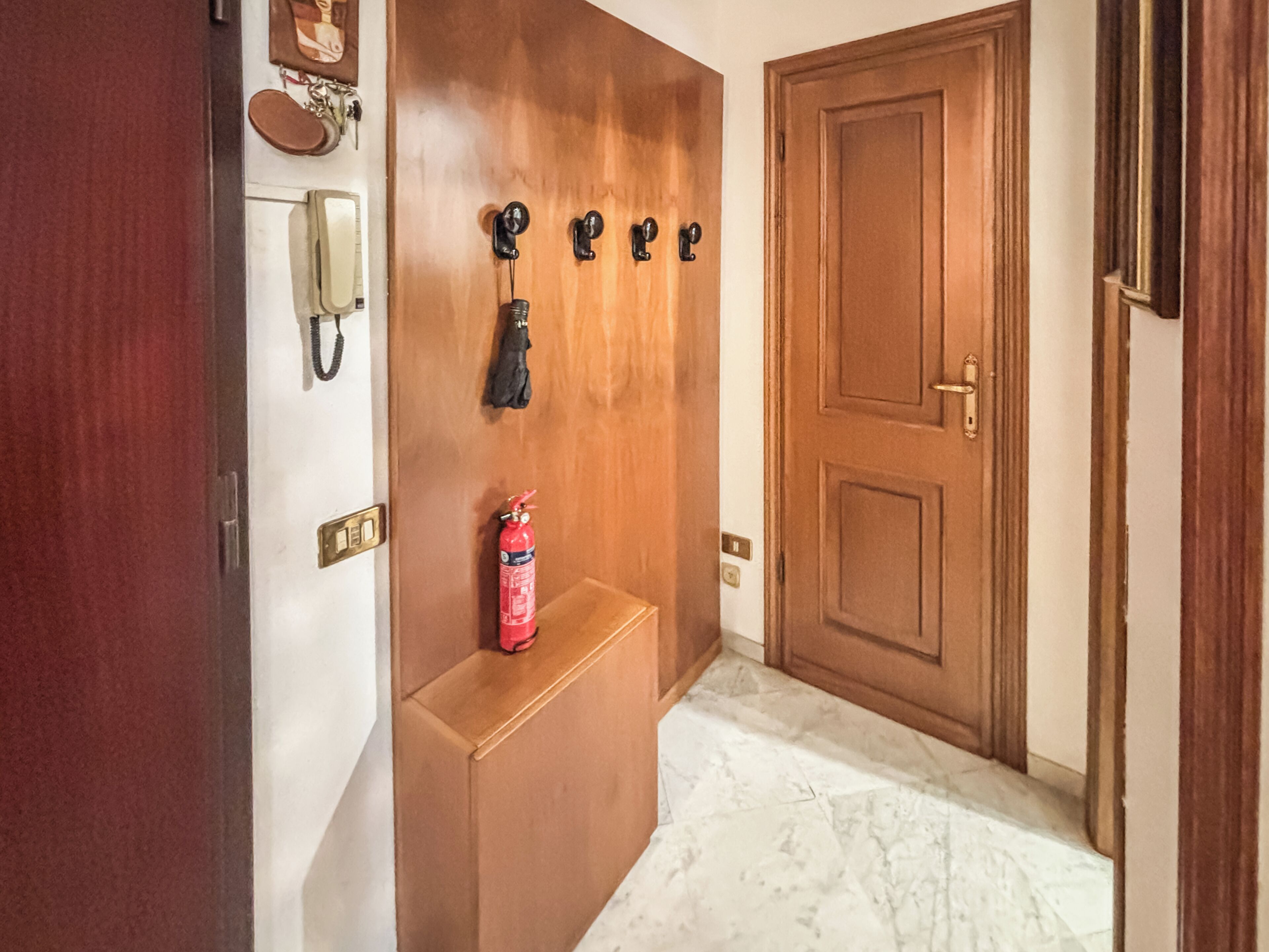 A hallway with a wooden door, a fire extinguisher, a coat rack, and a telephone.